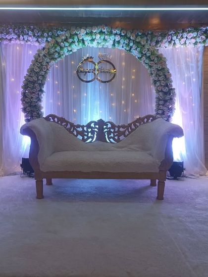 A classic ring ceremony stage with a full floral arch and a custom sign featuring interlocking rings. The white carpet and traditional sofa create a clean and elegant look.