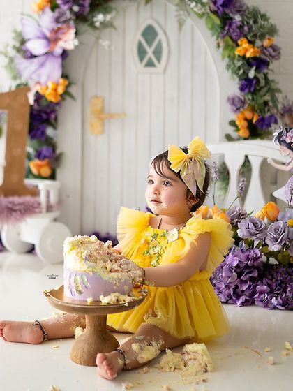 A first birthday cake smash in a magical fairy garden! This little one is enjoying her cake surrounded by purple and yellow flowers.