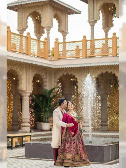 A romantic moment by a courtyard fountain, with beautiful palace architecture in the background. The groom whispers to his bride, creating a candid and sweet memory.