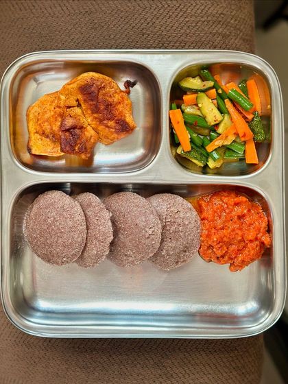 This plate features ragi idlis with pan-fried fish, sautéed vegetables, and a tomato chutney, offering a unique and healthy combination.