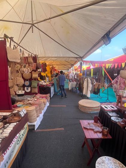 A view down an aisle of the Dastkar Bazaar, showing a variety of stalls under a covered structure. I focus on creating a logical flow and ensuring all vendors are visible and accessible.