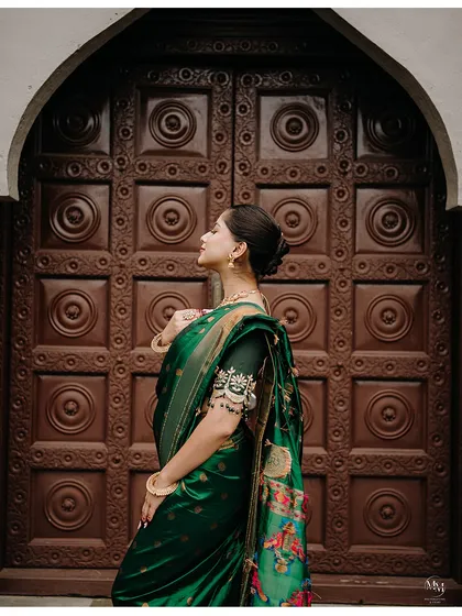 A side profile of a bride in her traditional green saree, standing before an ornate wooden door. This shot emphasizes her elegance and the rich cultural setting.
