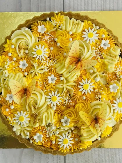A top-down shot of the yellow butterfly and daisy tart, showcasing the dense and detailed decoration that covers the entire surface. It's a bright and sweet work of art.