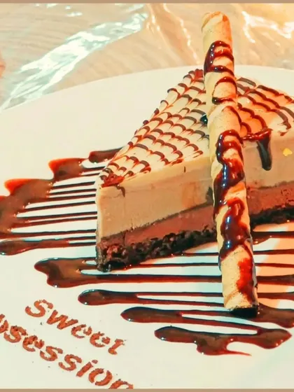 This is a slice of our rich cheesecake, drizzled with chocolate sauce. It's one of the many sweet indulgences you can enjoy when you visit.