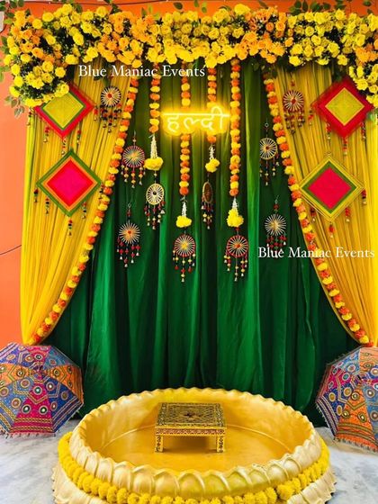 A traditional Haldi backdrop with green and yellow drapes, adorned with colorful hangings and umbrellas.