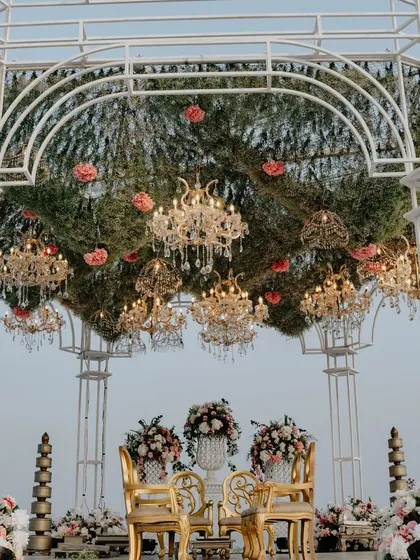 The intricate details of the mandap's floral canopy are visible here, with golden chandeliers nestled amongst a thick layer of hanging foliage and pink blooms.