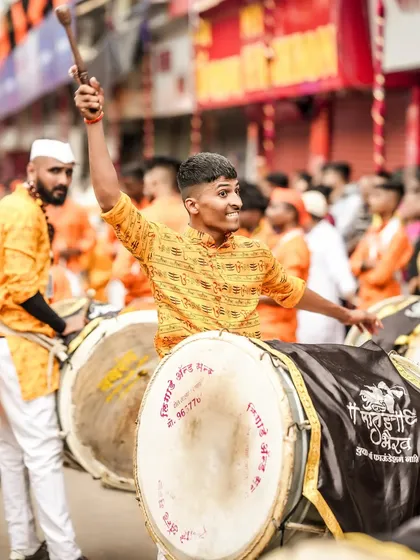 A dhol player raises his stick with passion and energy, his expression showing complete immersion in the music.