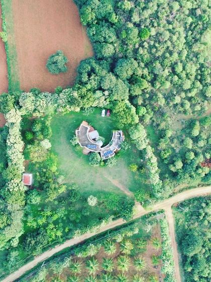 A wider aerial shot of the farmhouse, emphasizing how it is nestled within its own private green clearing, surrounded by fields and forests. The design truly respects and merges with the rural landscape.