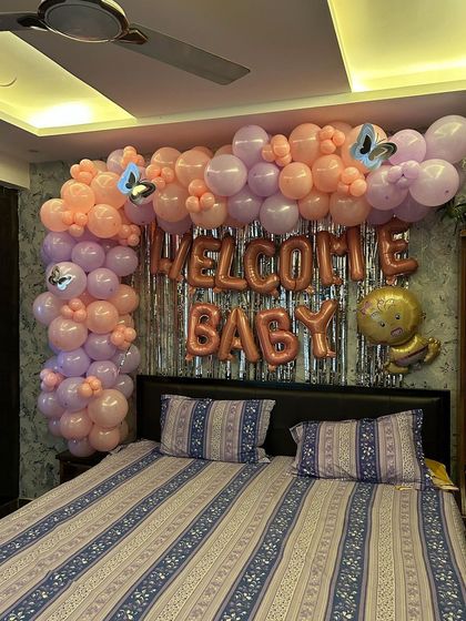 A sweet 'Welcome Baby' room decoration for a baby girl, using a pastel pink and purple balloon arch over the bed.