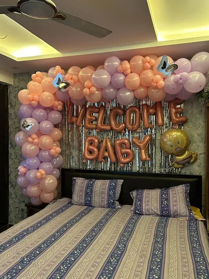 A sweet 'Welcome Baby' room decoration for a baby girl, using a pastel pink and purple balloon arch over the bed.