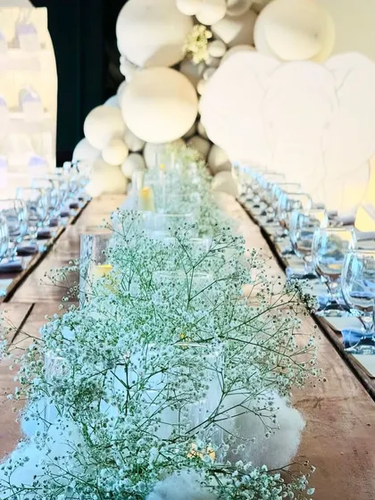 An exquisitely set dining table for a first birthday. The centerpiece is a runner of fluffy cotton and baby's breath, creating a dreamy, cloud-like effect.
