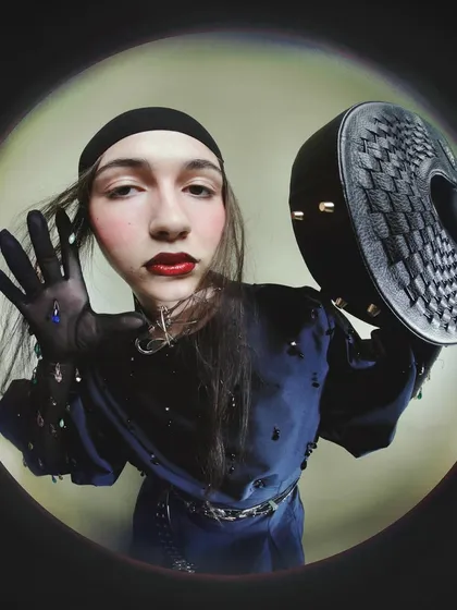 Another fisheye portrait where the model interacts with a textured handbag. The distorted perspective brings the viewer into the model's personal space.