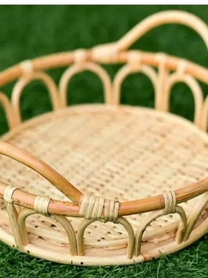 This round decorative tray is made from cane and rattan, featuring an openwork design around the edge and convenient handles. It is perfect for serving drinks or as a stylish organizer on a coffee table or ottoman.