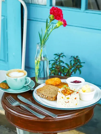 A simple and elegant breakfast setting with a cup of cappuccino and a plate of eggs and toast, set against a bright blue wall. This shot evokes a peaceful morning at a chic cafe.