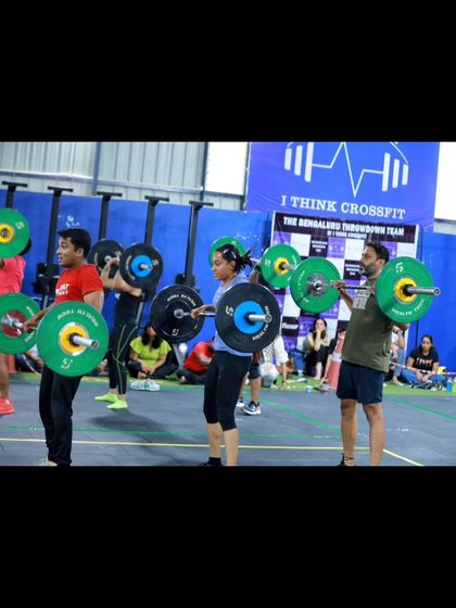 Multiple athletes holding heavy barbells in the front rack position during a synchronized squat event.