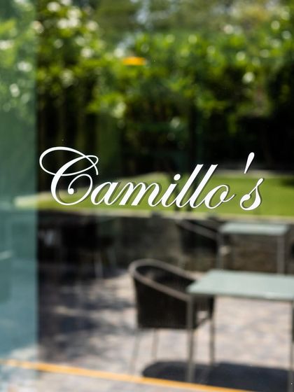 A glimpse of our outdoor seating area through the glass door, with the lush greenery of the garden just beyond. This is the view that welcomes you to your neighborhood artisanal pizzeria.