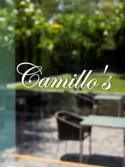 A glimpse of our outdoor seating area through the glass door, with the lush greenery of the garden just beyond. This is the view that welcomes you to your neighborhood artisanal pizzeria.