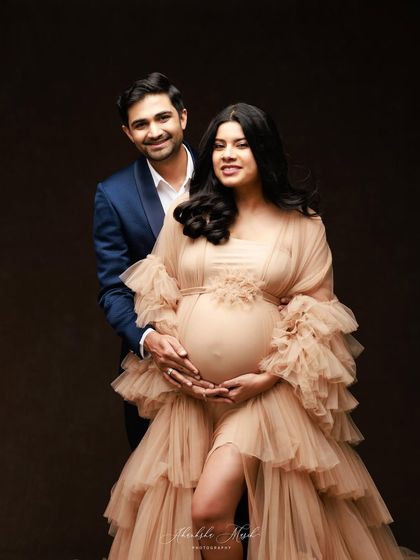 A smiling and confident couple's portrait, with the partner's arms wrapped lovingly around the mother-to-be.