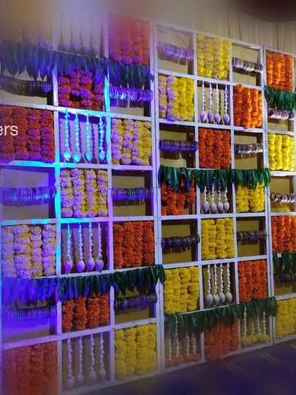 An angled view of the floral grid wall, showcasing the depth and texture created by the different flowers and hanging jasmine strings. The blue uplighting adds a modern touch to the otherwise traditional baby shower decoration.