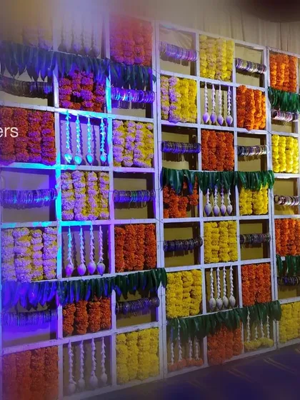 An angled view of the floral grid wall, showcasing the depth and texture created by the different flowers and hanging jasmine strings. The blue uplighting adds a modern touch to the otherwise traditional baby shower decoration.