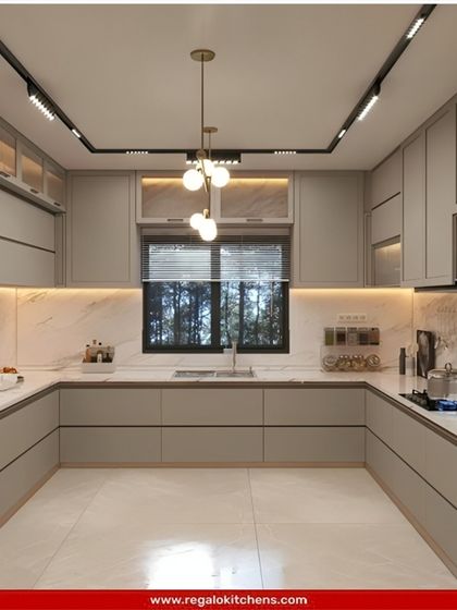 This bright and airy U-shaped kitchen is perfect for a modern home. The light grey cabinets, marble backsplash, and large window create a spacious feel. Track lighting and spotlights ensure the entire area is perfectly illuminated.