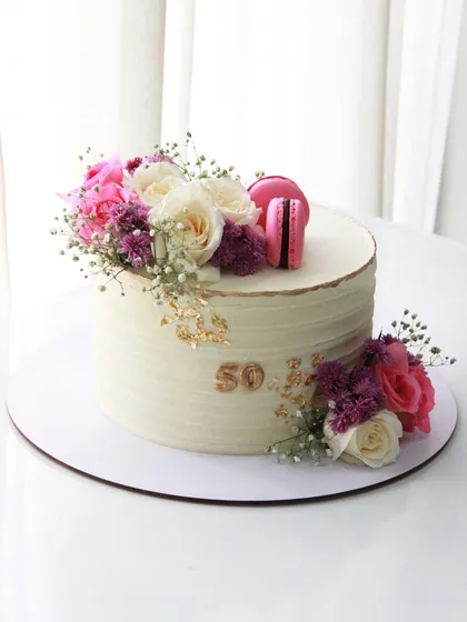 Celebrating five decades with a touch of floral elegance. This 50th birthday cake features a textured buttercream finish, gold leaf accents, and a beautiful arrangement of fresh flowers and macarons.