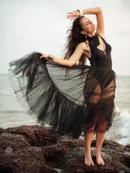 A powerful and expressive pose on the rocks, with the model's hair and the black skirt blowing in the wind. This shot is full of energy and drama.