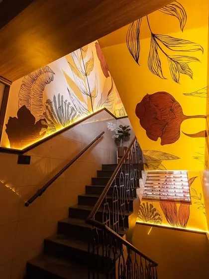 The warm, yellow-themed staircase, illuminated by subtle strip lighting and a cascade of bamboo pendants. The hand-painted murals make this transitional space a destination in itself.