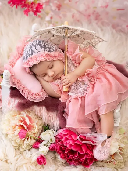 A sleeping beauty surrounded by a bed of flowers. This elaborate floral setup in shades of pink, complete with a lace bonnet and parasol, creates a truly enchanting and delicate newborn portrait.