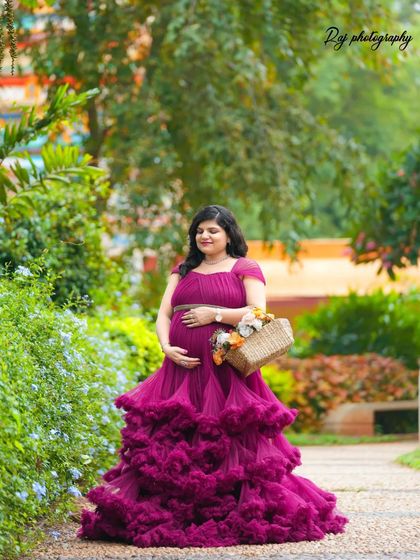 A beautiful solo portrait of a mother-to-be in a wine-colored ruffled gown, walking down a garden path.