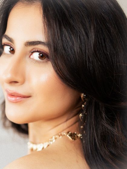 A beautiful close-up beauty shot. The focus is on the model's glowing skin, natural makeup, and the delicate jewelry, highlighting a look of effortless elegance.