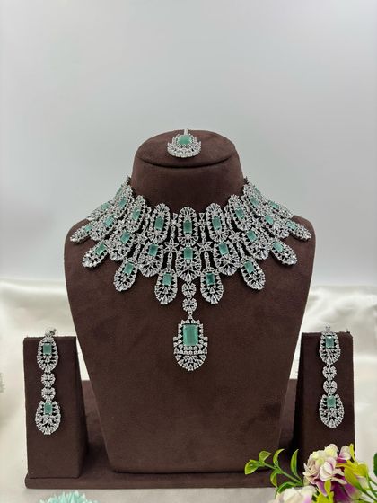 A full-coverage AD bridal set with a matching maang tikka. This silver-plated design is available in a wide range of colors like green, blue, pink, and white, making it a versatile choice for weddings.