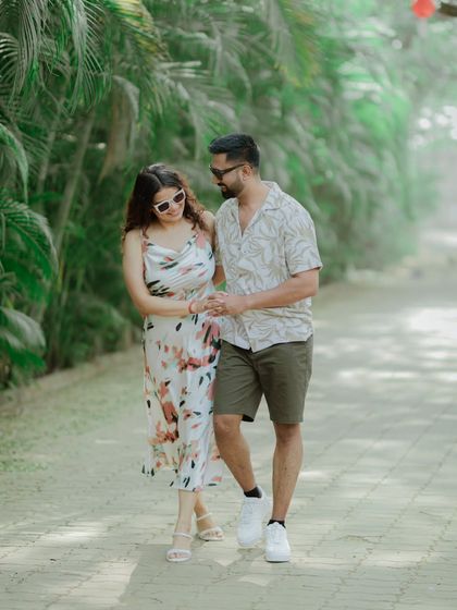 A couple in casual, summery outfits enjoys a walk through a path lined with palm trees. This image feels natural, relaxed, and perfect for a vacation-style shoot.