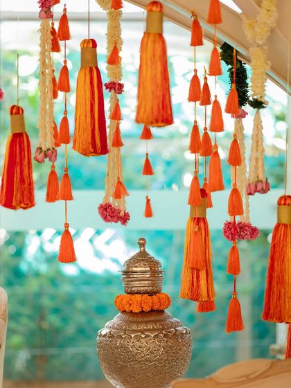 A detail shot of hanging orange tassels and floral strings, adding a touch of traditional whimsy to a modern Mehendi setup.