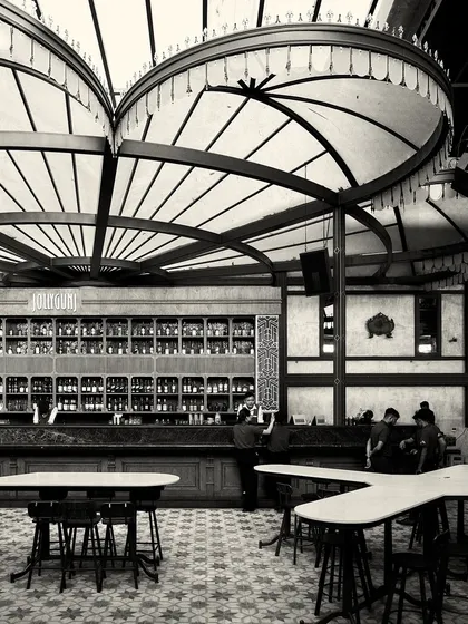 The main bar area with its unique tables and high stools. The patterned floor and grand light fixtures are prominent in this grayscale shot.