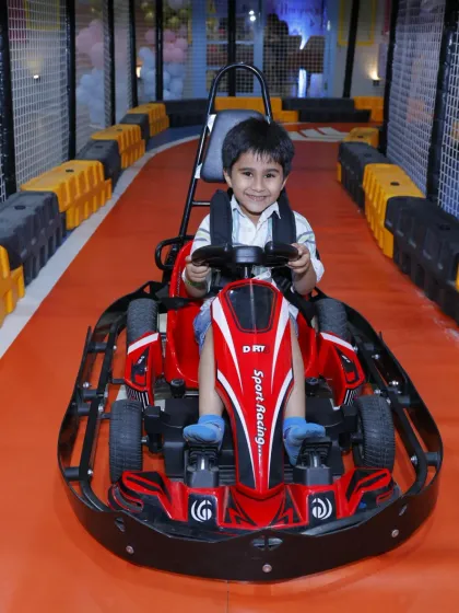 A happy boy gives a big smile from his red go-kart, excited for the race to begin.