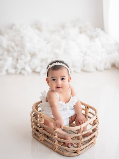 A happy baby girl in a wicker basket, set against a backdrop of fluffy white clouds.