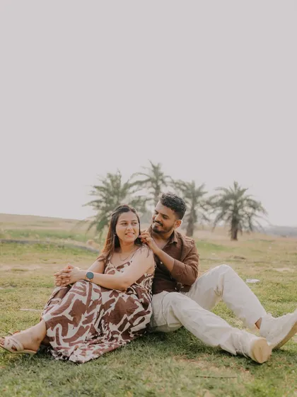 A relaxed portrait of the couple sitting in a field with palm trees in the background. Their comfortable pose and loving gaze make this a sweet and natural shot.