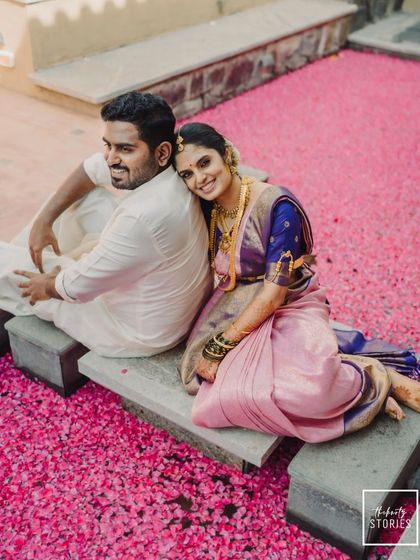 A high-angle view of a couple finding a quiet moment together. The vibrant pink flower petals create a stunning contrast with their traditional outfits, making for a memorable shot.
