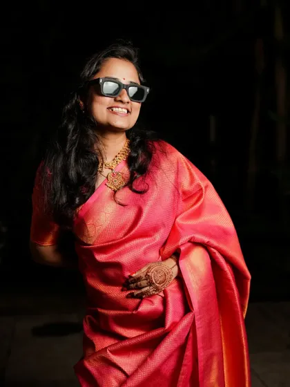 A playful portrait of a woman in a vibrant pink saree, wearing sunglasses and smiling, capturing a fun 'Nakhra' swag.