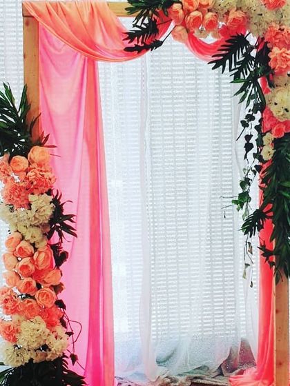 This simple wooden arch, decorated with peach and white flowers and flowing pink fabric, is a lovely setup for a naming ceremony cradle. The design is soft, elegant, and perfect for celebrating a new arrival.