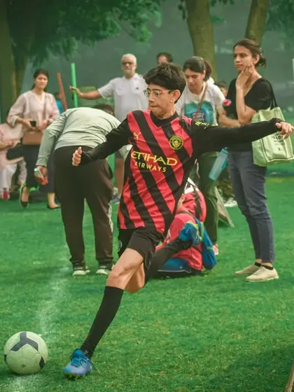 A player takes a free kick, with parents watching in the background.