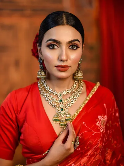 A detailed close-up of a bride's makeup, highlighting the flawless skin, bold lip, and intricate jewelry. This is a perfect reference shot for clients looking for a classic red-themed bridal look.