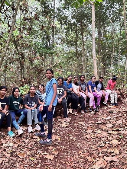 A larger group of female campers takes a break on a fallen log during a hike through the Dandeli forest.