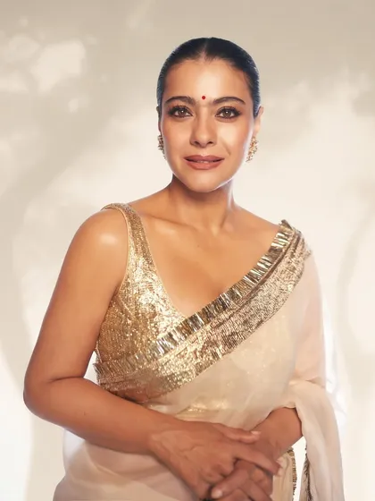 A close-up of Kajol radiating elegance in a luminous white saree with a shimmering gold sequin blouse for a movie premiere.