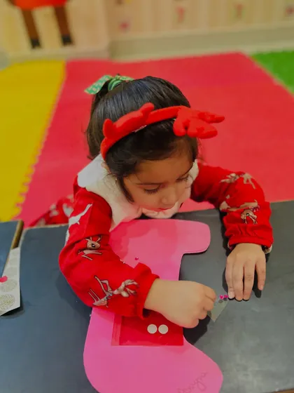 A girl in a reindeer headband works diligently on her stocking craft.