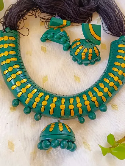 A very pretty 'hansli' style necklace in green and gold. This piece has a simpler, painted design and comes with a full set of matching earrings and a central hanging jhumka.