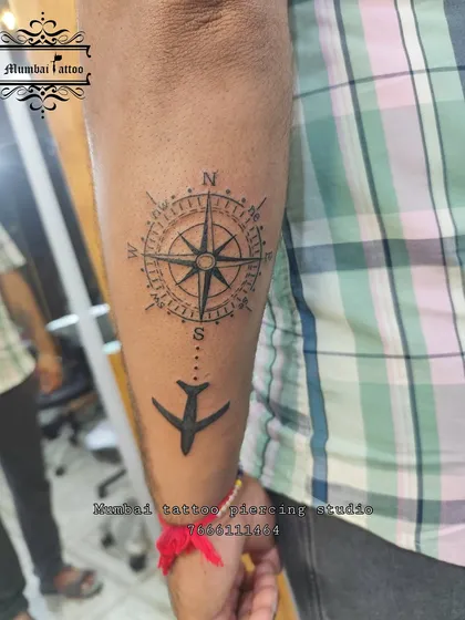A still image of the compass and airplane travel tattoo. The combination of the detailed compass and the simple, bold airplane creates a balanced and visually appealing design.