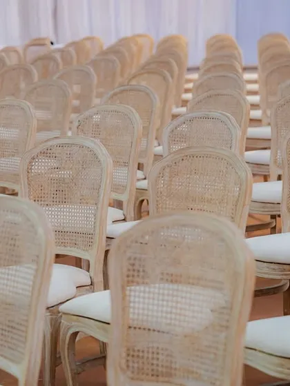 Rows of elegant cane-back chairs await guests at this sustainable wedding. The choice of natural, reusable materials like cane and wood reinforces the eco-friendly ethos of the event without compromising on style.