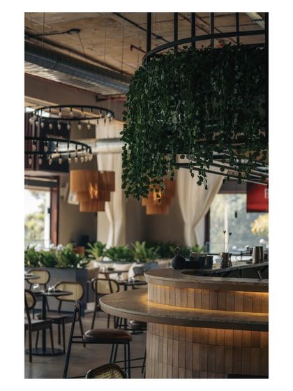 A close-up of the bar area, where hanging greenery softens the industrial grid structure above. The warm under-counter lighting highlights the texture of the subway tiles.